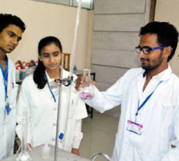 Three persons wearing lab coats gather around a beaker, conducting experiments in a laboratory.