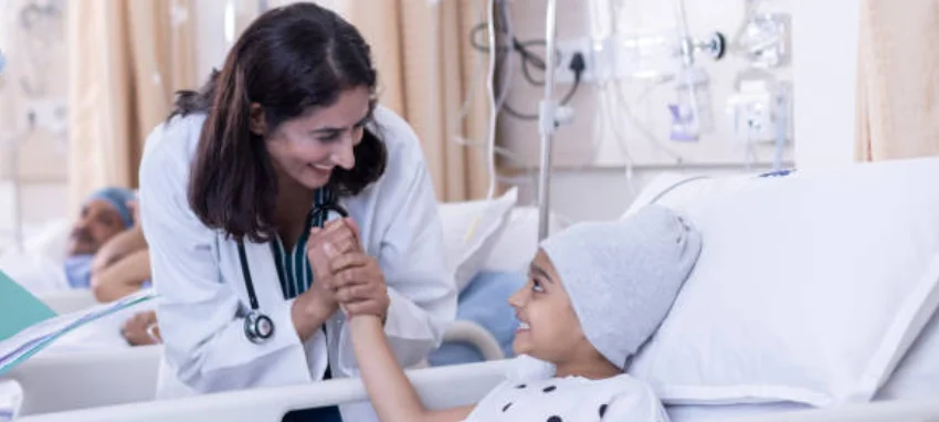 A woman in a hospital room gently holds a child's hand, providing comfort and support