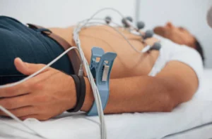 A man on a bed with a cardiology device attached to his chest, monitoring his heart health.
