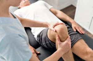 A physical therapist examining a patient's knee in a physiotherapy setting.
