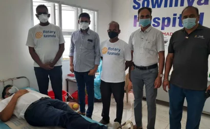  A man on a bed giving blood while holding a ball in his hands, 5 other men are standing next to him